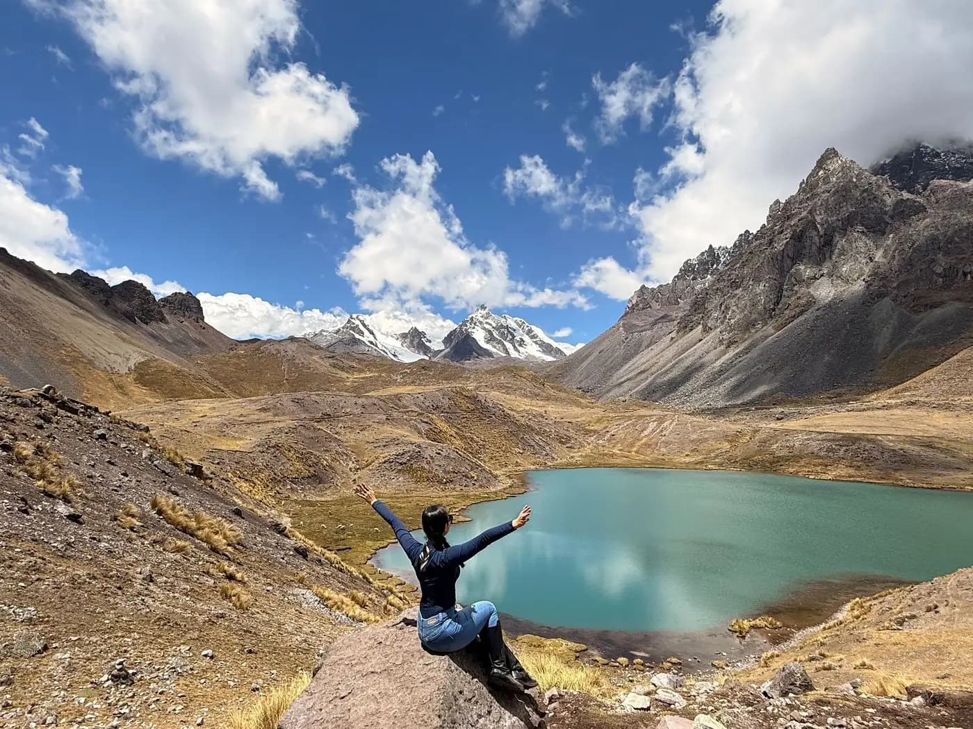 Hiker with arms raised above a turquoise lake on the Ausangate 7 Lakes hike, Peru